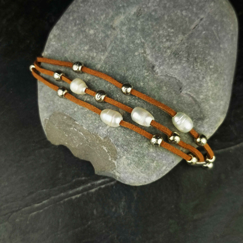 Wit zoetwater parel armband met bruin leer en magneetslot liggend op kei | Aafke