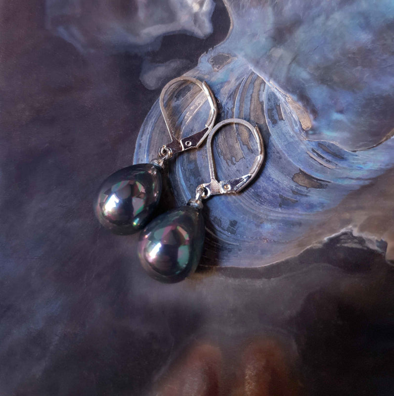 Petroleum kleurige parel oorbellen in druppel vorm met zilver edelstaal liggend in schelp