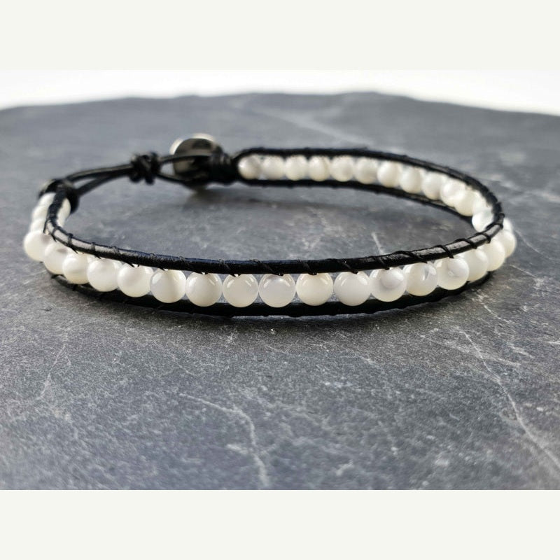 Parelmoeren armband met wit parelmoer en zwart leer liggend op leisteen | White Shell Wrap