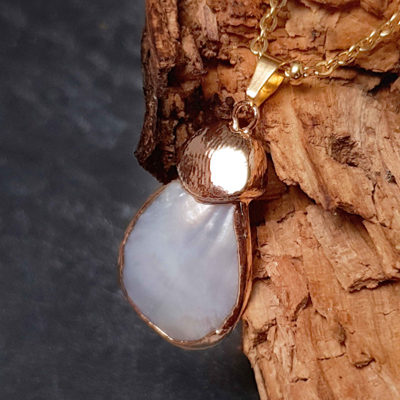 Detail van witte parelmoeren ketting met wit parelmoer hanger aan gouden edelstalen ketting hangend aan hout | Gold Shell