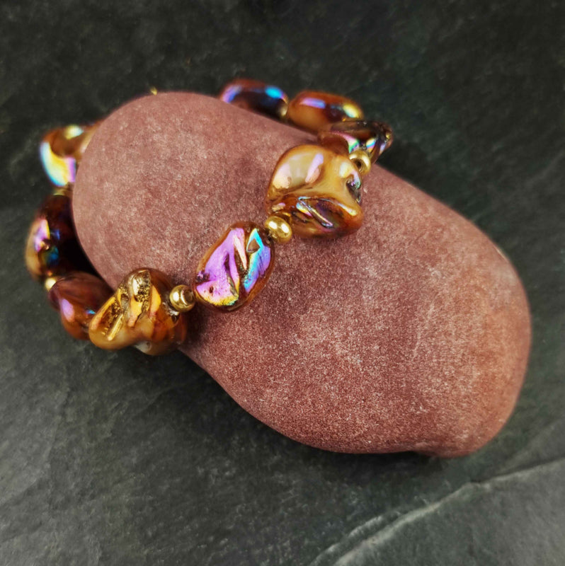 Bruin parelmoeren schelpen armband met goud edelstaal liggend op rode kei | set Shell AB Brown Gold