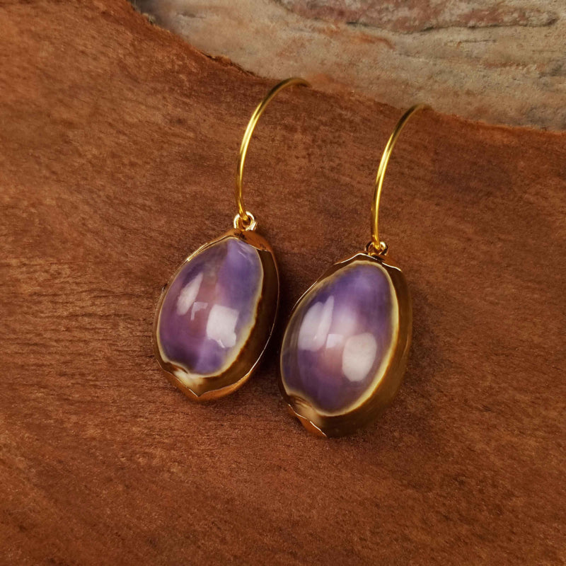 Gouden oorringen met paarse schelpen en goud edelstaal hangend aan hout | Shell Cowrie Purple