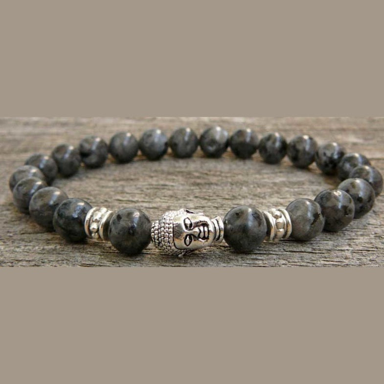 Edelstenen armband met zwarte edelstenen en een Boeddha hoofd liggend op hout | Elastisch | Buddha Larvikite