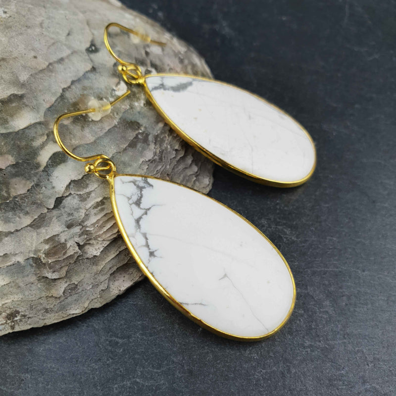 Witte edelstenen oorbellen met howliet en goud edelstaal liggend tegen schelp | Big Teardrop Howlite Gold