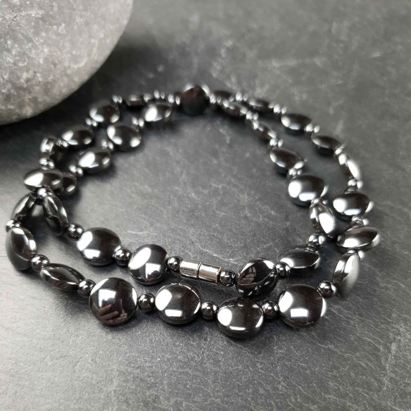 Zwarte edelstenen ketting met hematiet en magneetslot opgerold liggend op leisteen| Hematiet Coin