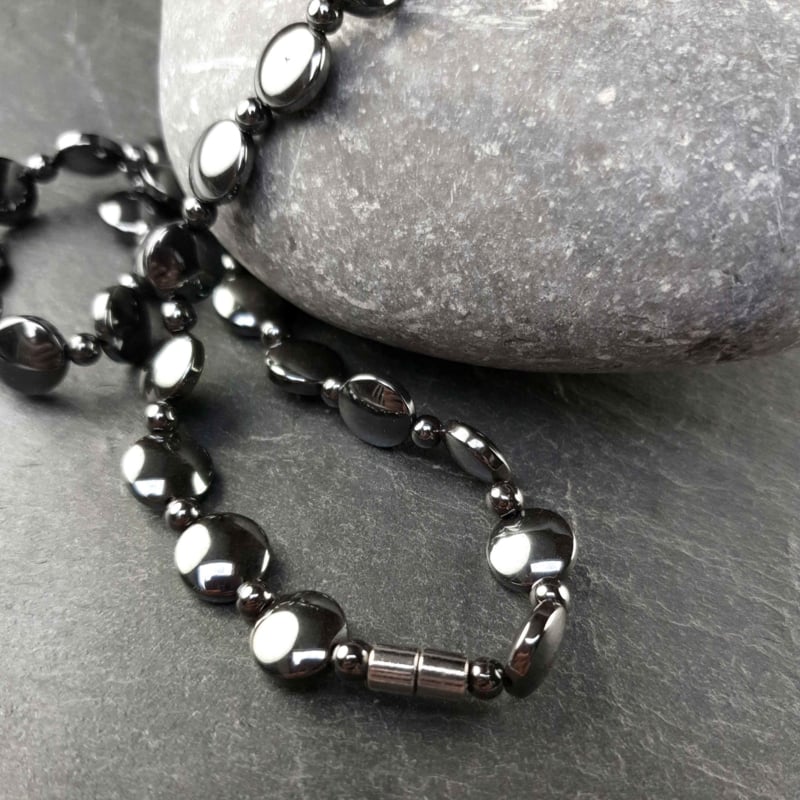 Zwarte edelstenen ketting met magneetslot en hematiet stenen liggend op grijze steen | set Hematite Coin
