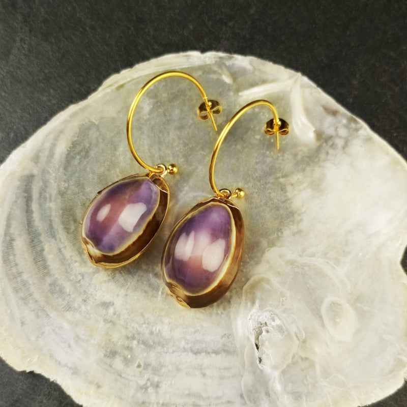 Schelpen oorbellen met paarse schelp en goud edelstaal liggend op witte schelp | set Shell Cowrie Purple