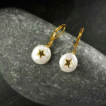 Witte zoetwater parel oorbellen met goud edelstaal en parel hanger met gouden ster liggend op grijze steen | set Coin Pearl Golden Star
