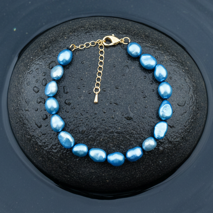Blauw zoetwaterparel armband met goud edelstalen slotje is volledig handgeknoopt en ligt op een steen in water | Blair