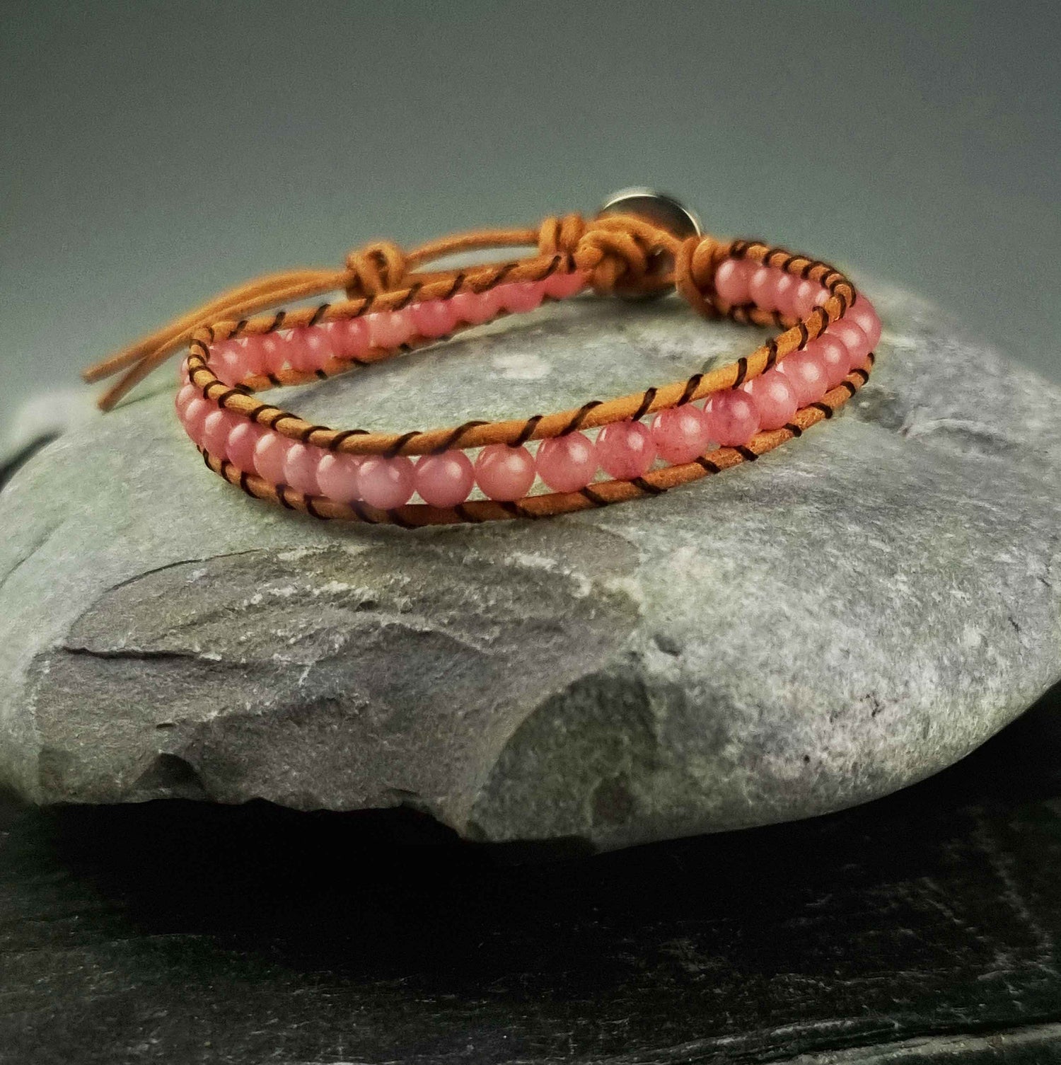 Roze edelstenen armband met rozenkwarts en bruin leer vooraanzicht liggend op kei | Wrap Little Rose Quartz