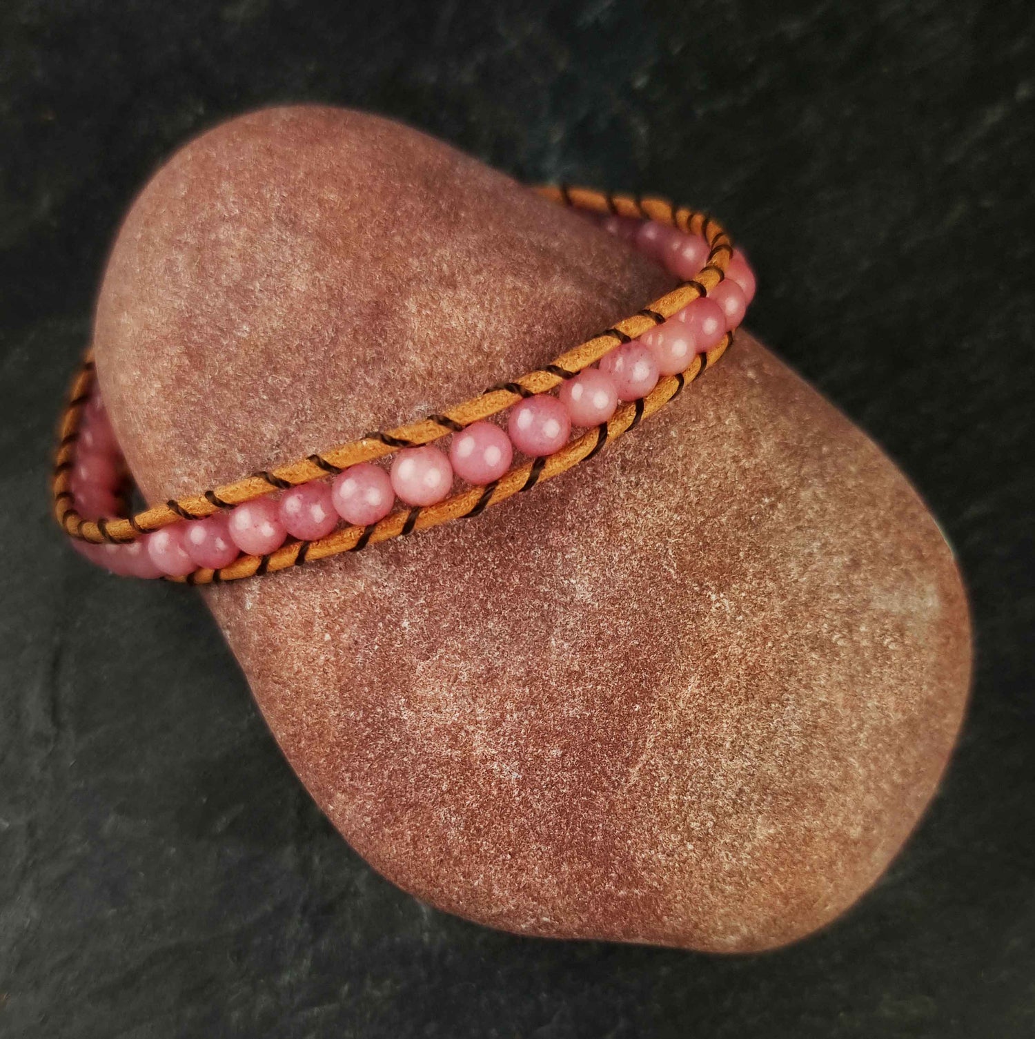 Roze edelstenen armband met rozenkwarts en bruin leer liggend op rode steen | Wrap Little Rose Quartz