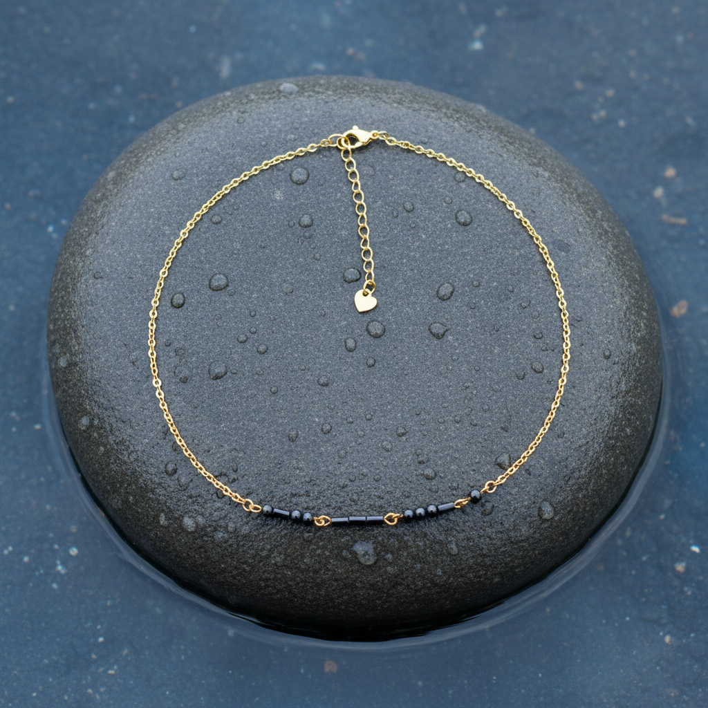 Zwarte edelstenen ketting met goud edelstaal en hematiet stenen die het woord LOVE in morse code weer geeft  liggend op steen in water | Morse Code Love Black Hematite Gold