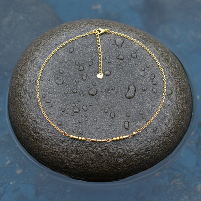 Gouden edelstenen ketting met goud edelstaal en hematiet stenen die het woord LOVE in morse code weer geeft liggend op steen in water | Morse Code Love Gold 