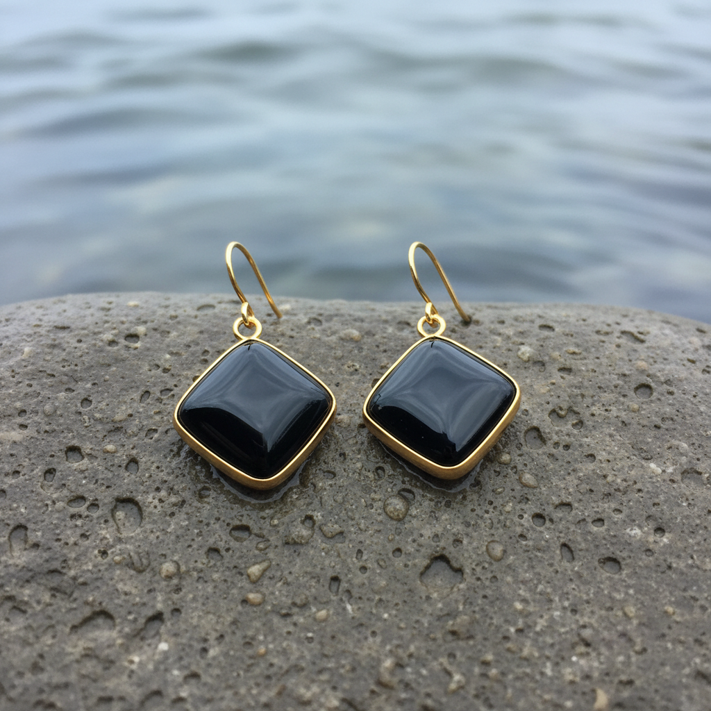 Zwarte dekstenen oorbellen met goud edelstaal liggend op natte steen | Blacke Agate Gold Square