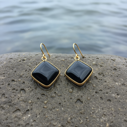 Zwarte dekstenen oorbellen met goud edelstaal liggend op natte steen | Blacke Agate Gold Square