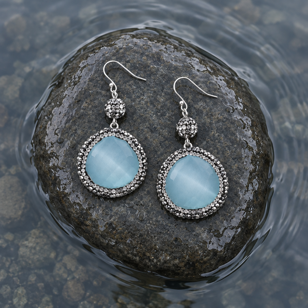 Licht blauwe edelstenen oorbellen met kattenoog, stras steentjes en sterling zilver (925) liggend op steen in water | Bright Blue Cat’s Eye