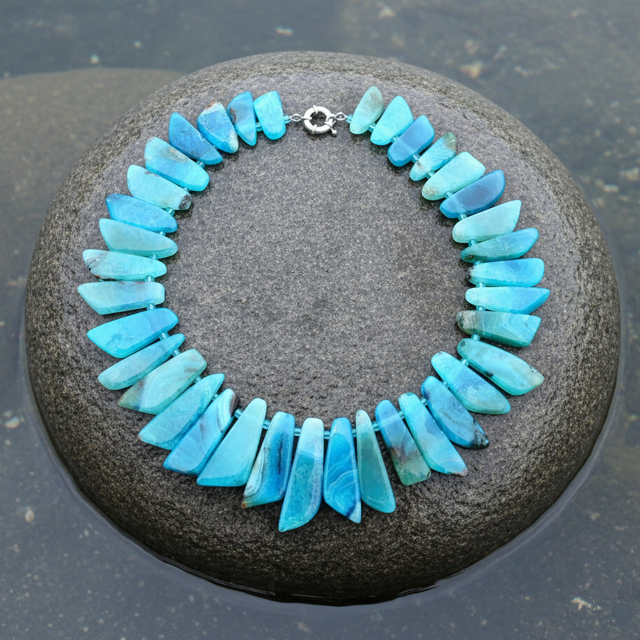 Close-up bovenaanzicht ketting met turquoise blauwe agaat stenen plakjes op grote grijze steen met natuurlijk blauw-grijs meerwater