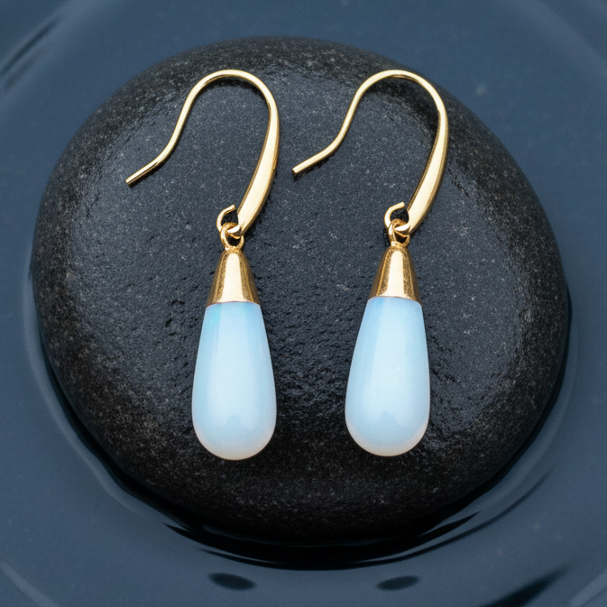 Licht blauwe edelsten oorbellen met opaal liggend op steen in water | Long Gold Dip Sea Opal