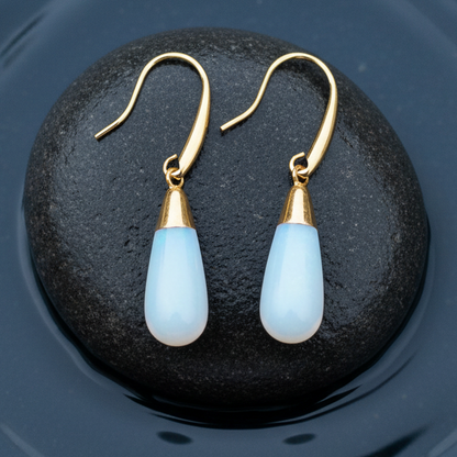 Licht blauwe edelsten oorbellen met opaal liggend op steen in water | Long Gold Dip Sea Opal