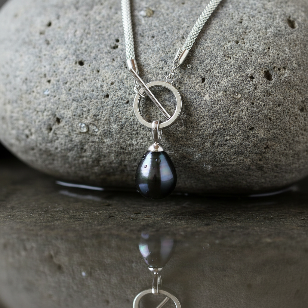 Slotje van mother of pearl parelketting met zwart groene parel hanger liggend op steen | Zora