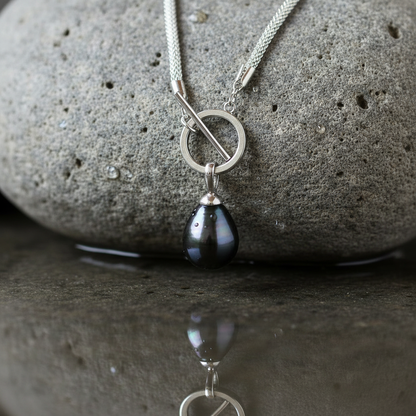 Slotje van mother of pearl parelketting met zwart groene parel hanger liggend op steen | Zora