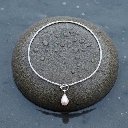 Detail van roze parelketting met parelhanger en zilver edelstaal liggend op steen | Mora