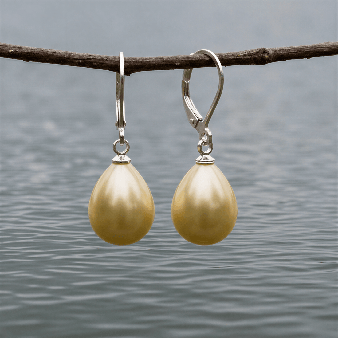 Gele mother of pearl parel oorbellen met zilver edelstaal hangend aan takje boven water | Lolly