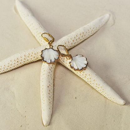 Witte parelmoeren oorbellen in de vorm van een shell schelp met goud edelstaal liggend op strand | Smalle Gold Sea Shell