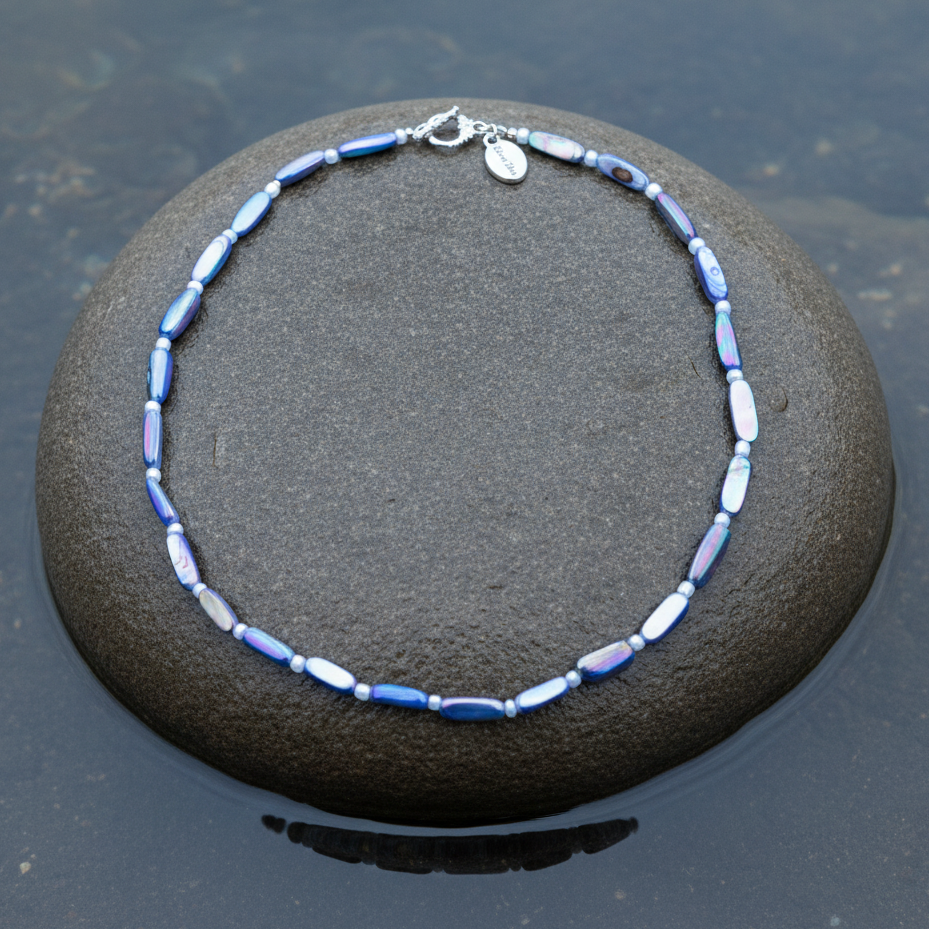 Blauwe parelmoeren ketting liggend op steen in water | Shell Stick AB Blue
