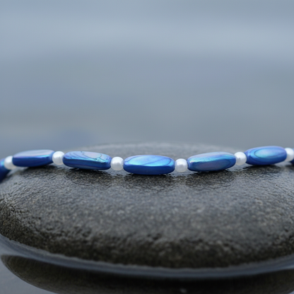 Blauwe parelmoeren ketting liggend op steen in water close up | Shell Stick AB Blue