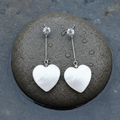 Witte parelmoeren oorbellen met wit parelmoer hartje, stras steen en zilver edelstaal liggend op steen | Bling Long White Shell Heart
