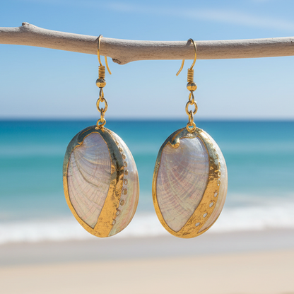 Parelmoeren schelpen oorbellen met witte schelp en goud edelstaal hangend aan takje met achtergrond zee | oorbellen White Shell Gold