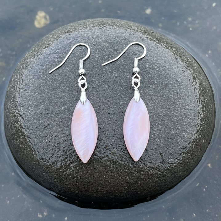 Close-up bovenaanzicht roze parelmoeren oorbellen plat liggend op grijze steen met natuurlijk blauw-grijs meerwater