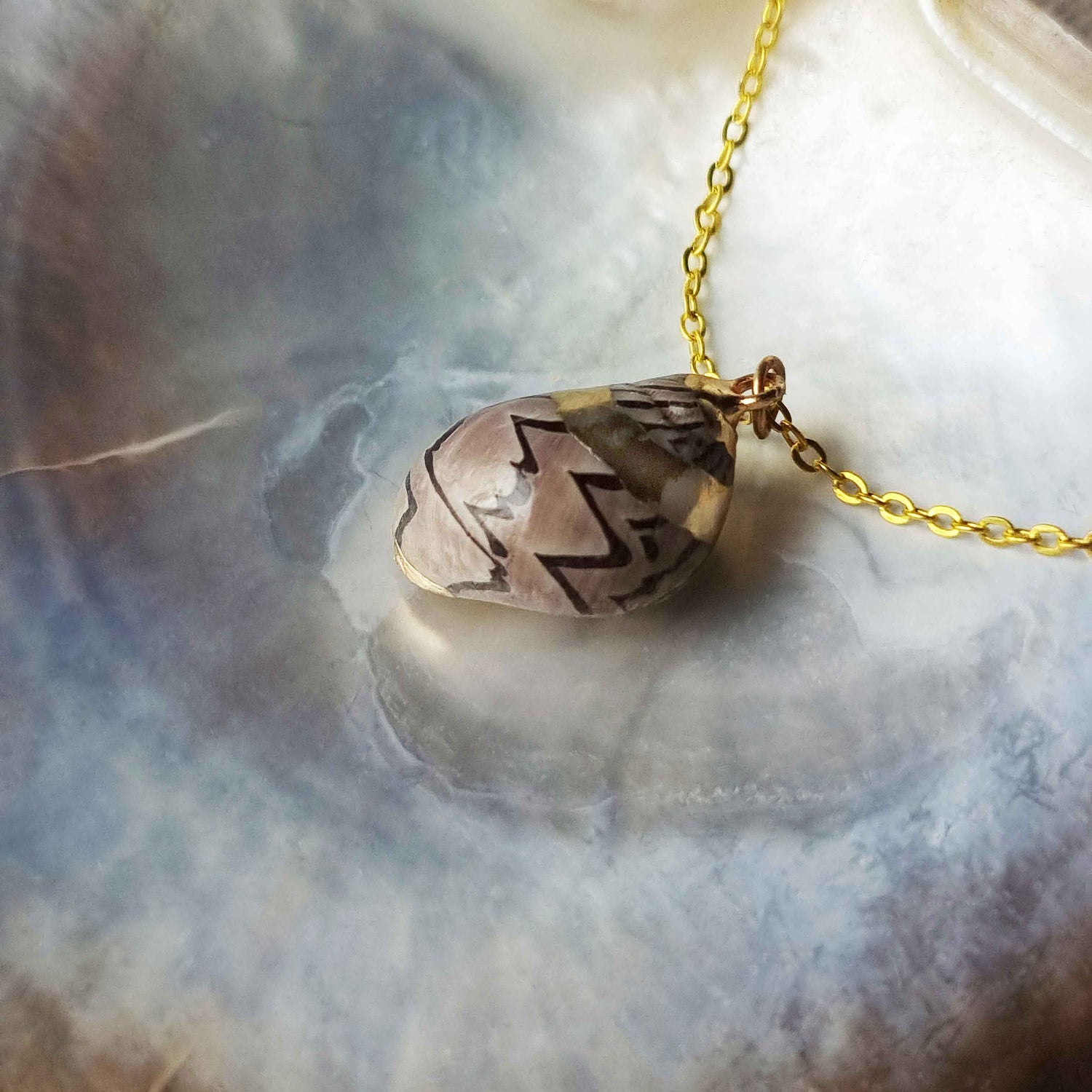 Detail van gouden schelpen ketting met bruine schelp liggend in schelp | Gold Spiral Shell