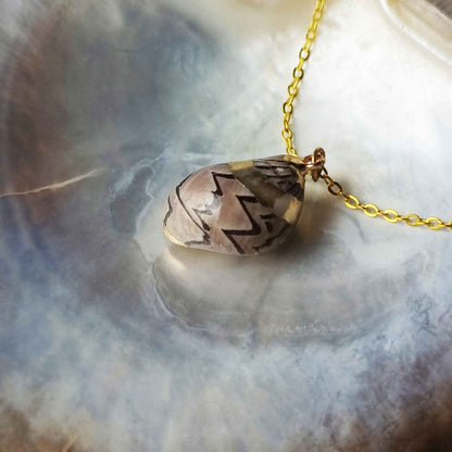 Detail van gouden schelpen ketting met bruine schelp liggend in schelp | Gold Spiral Shell