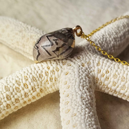Detail van gouden schelpen ketting met bruine schelp liggend op zeester | Gold Spiral Shell