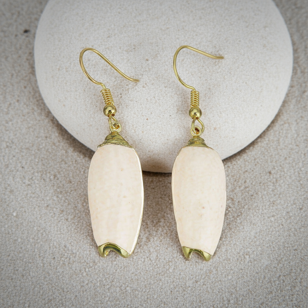 Schelpen oorbellen met beige schelp en goud edelstaal liggend tegen steen op het strand | Pillar Seashell Gold