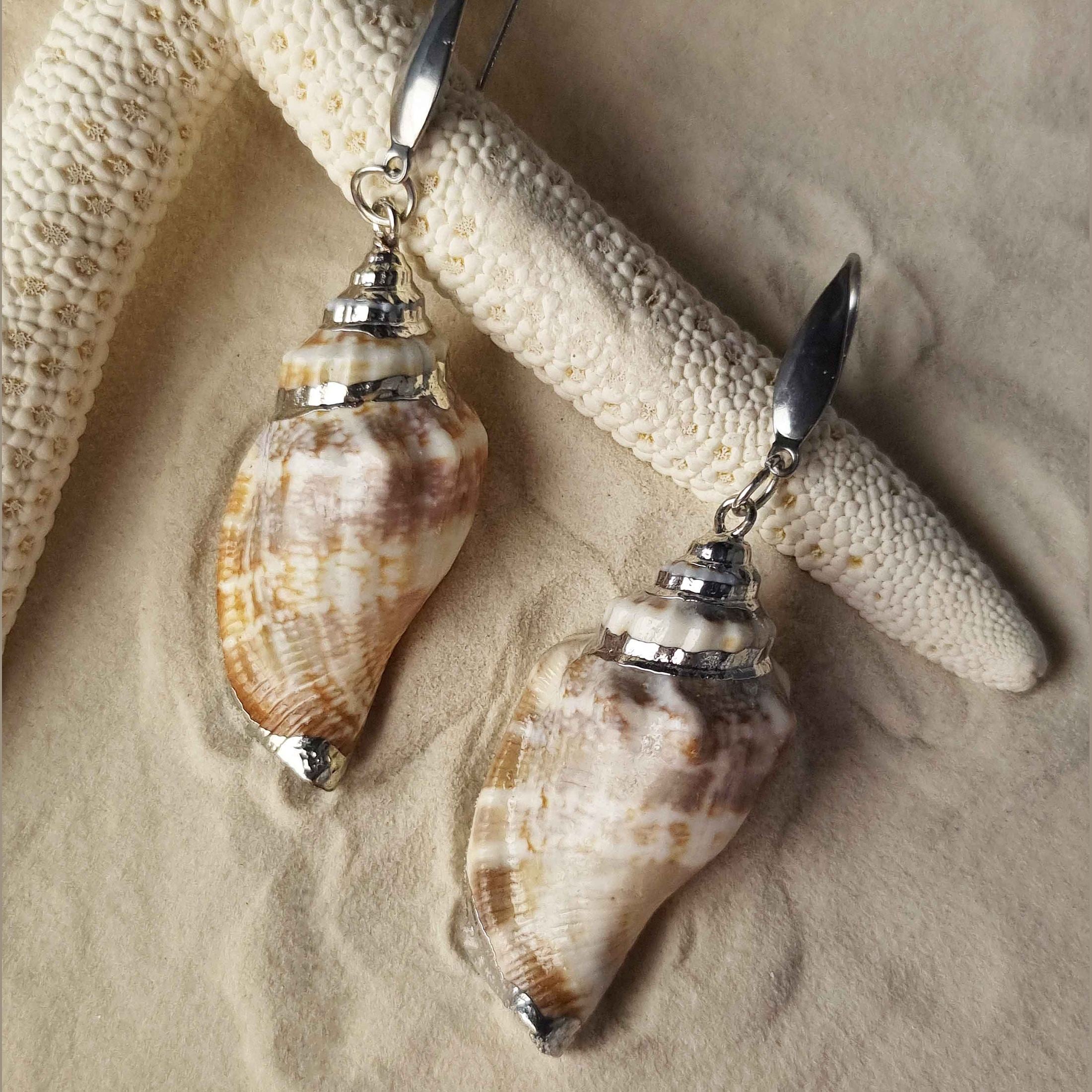 Schelpen oorbellen met wit en beige schelp met zilver edelstaal liggend op zand | Seashell Silver