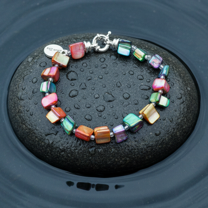 Bont gekleurde parelmoeren schelpen armband liggend op steen in water | Shell Chip AB Color