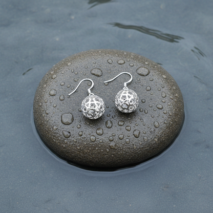 Verzilverde oorbellen met opengewerkte bol liggend op steen | Silver Ball