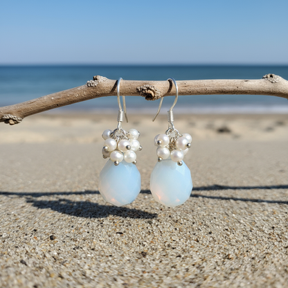 Witte zoetwater parel oorbellen met zee opaal en sterling zilver (925) hangend aan takje met achtergrond zee | Coline