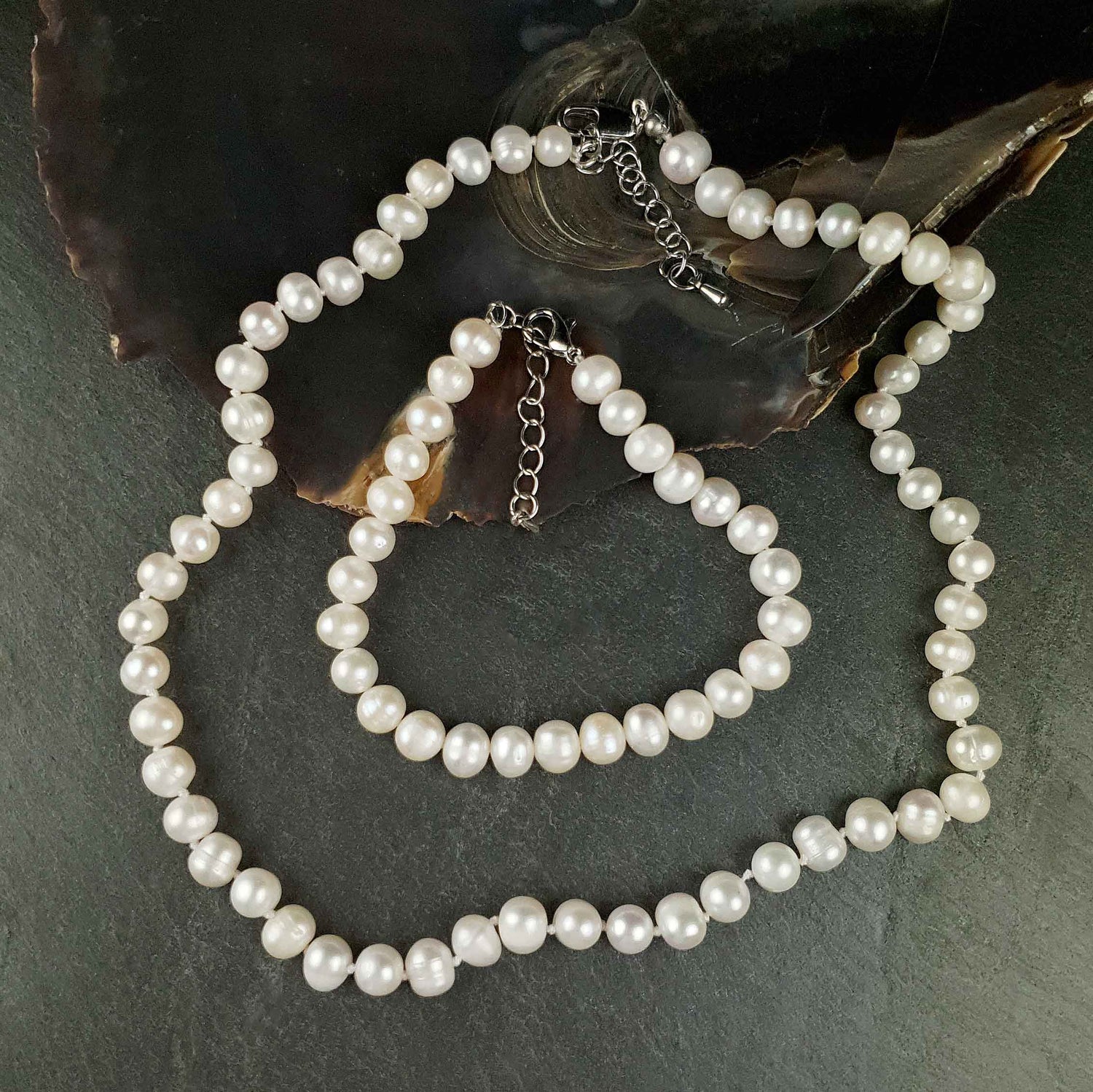 Witte zoetwater parel set met sterling zilveren slotjes bestaande uit een witte parelketting en een wit parel armband liggend op leisteen en schelp | set Bella (KA)