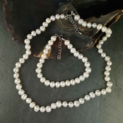 Witte zoetwater parel set met sterling zilveren slotjes bestaande uit een witte parelketting en een wit parel armband liggend op leisteen en schelp | set Bella (KA)