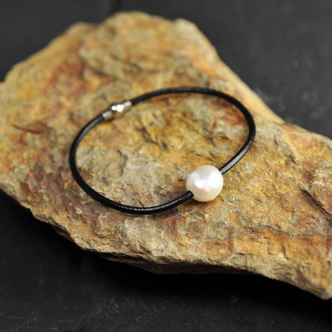Wit zoetwater parel armband met zwart leer en magneetslot liggend op oranje steen| Baliene