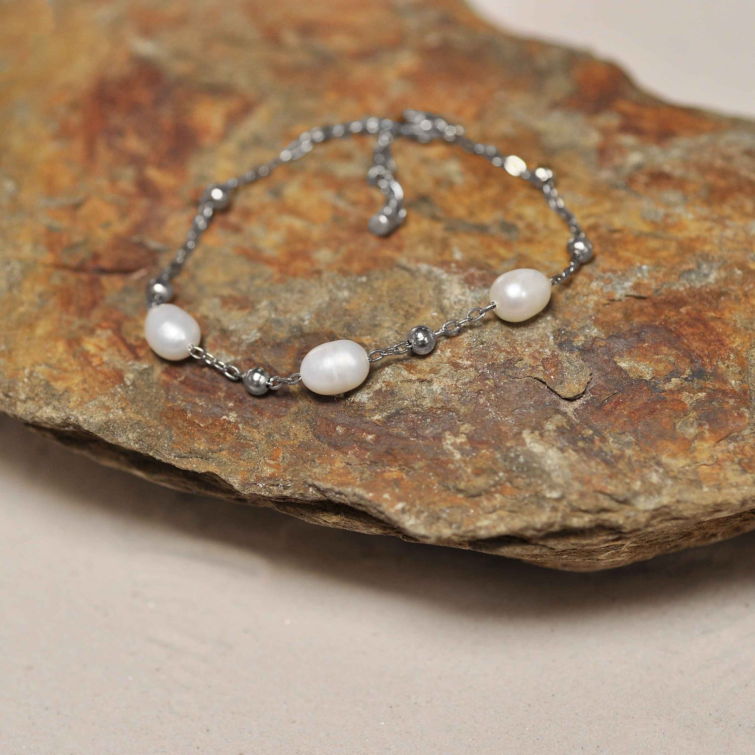Wit zoetwater parel armband met zilver edelstaal liggend schuin op steen | Parel armband Eline Zilver