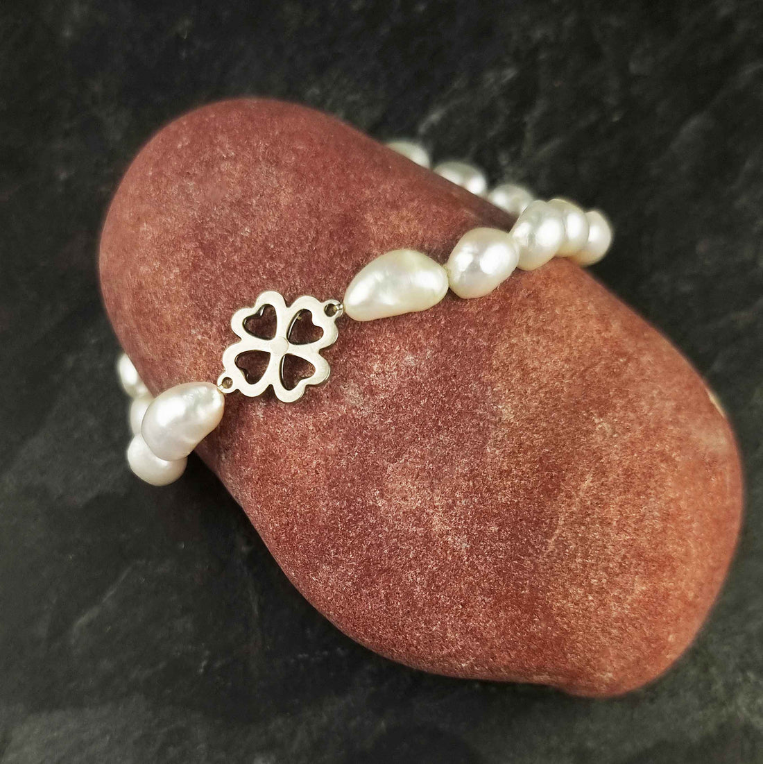 Wit zoetwater parel armband met een klavertje 4 van zilver edelstaal liggend op rode steen | Good Luck Groot Klavertje 4 Silver