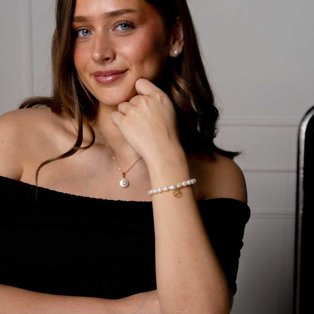 Wit zoetwater parel armband met gouden symbool sterrenbeeld boogschutter op model aan tafel | Parel armband Gouden sterrenbeeld Boogschutter