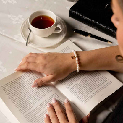 Wit zoetwater parel armband met gouden symbool sterrenbeeld boogschutter op model die boek leest  | Parel armband Gouden sterrenbeeld Boogschutter