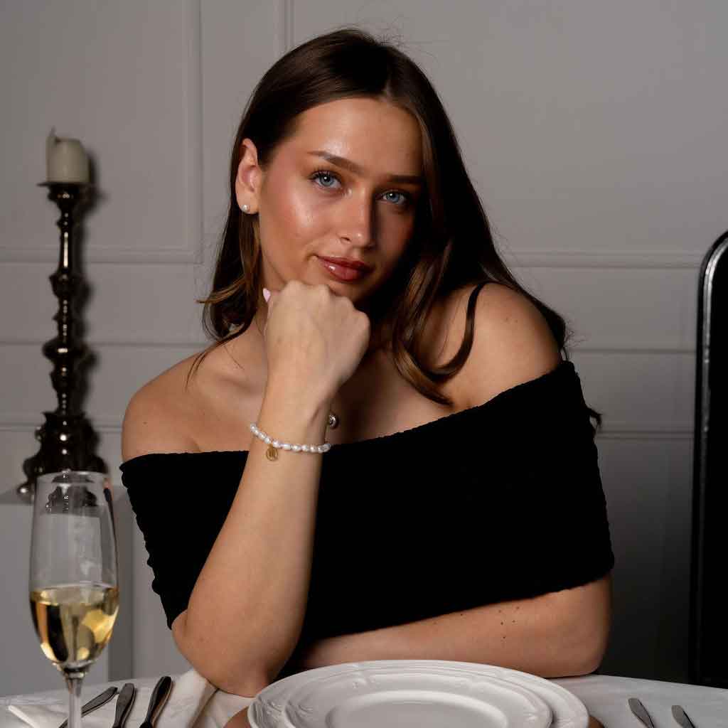 Wit zoetwater parel armband met symbool van sterrenbeeld schorpioen in edelstaal op model aan tafel | Gouden Sterrenbeeld Schorpioen