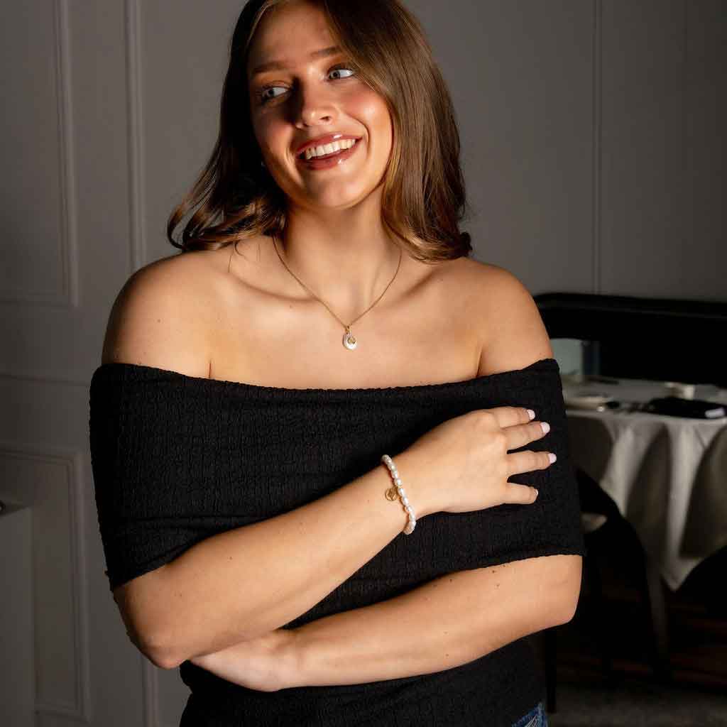 Wit zoetwater parel armband met symbool van sterrenbeeld schorpioen in edelstaal op model met jurk | Gouden Sterrenbeeld Schorpioen